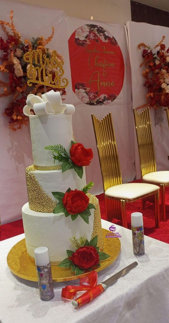 White and gold three-tier wedding cake with red roses, Kampala